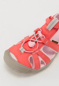 Korallig rosa sandal laget av stoff og gummimaterialer. Har justerbare stropper, et raskt snøresystem og pustende utskjæringer. Vaskbart design.