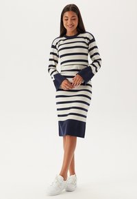 Gestreift gestricktes Kleid in Marineblau und Cremefarben, mit langen Ärmeln und breiten Bündchen, sowie einer figurbetonten Silhouette, die bis zum Knie reicht.