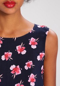 Marineblaues Kleid mit rundem Ausschnitt, verziert mit rosa Blumenmustern und grünen Blättern. Hat ein ärmelloses Design und eine glatte Textur.