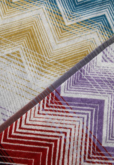 Multikleurige geweven stof met zigzagpatronen in geel, blauw, rood, paars en wit. Gevoelige oppervlakte met gedetailleerd stikwerk.