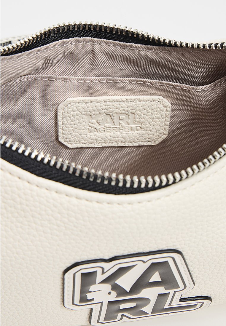 Pochette en cuir blanc texturé avec une fermeture éclair noire, intérieur en tissu beige, dotée d'une étiquette logo 'KARL LAGERFELD' et d'un accent logo noir et blanc.