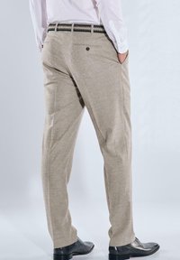 Hellbeige Hose mit leicht strukturierter Stoffqualität, ausgestattet mit Seitentaschen und einem gewebten schwarzen Gürtel, von hinten betrachtet.