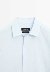 Chemise à rayures verticales bleu clair et blanc avec col ouvert, devant boutonné, et étiquette Massimo Dutti à l'intérieur du col.