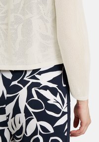 Crème-kleurige, textuur gebreide top met een ronde halslijn en lange mouwen. Gecombineerd met navy broek met een wit bloemenpatroon.