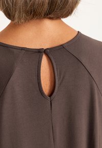 Donkerbruine kleding met een ronde halslijn en een sleufopening aan de achterkant. Glad van textuur, met schoudernaad.