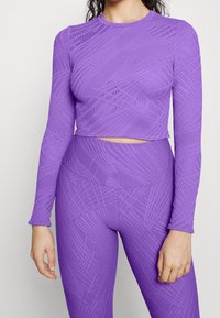Purple long-sleeve crop top and high-waisted leggings made of textured, stretchy material with geometric patterns across the fabric.