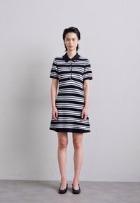 Striped black and white polo dress with short sleeves, button placket, and flared skirt. Worn with black flats. Smooth fabric texture.