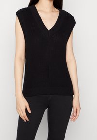 Svart stickad ärmlös topp med breda axelsömmar, djup V-ringning och ribbat mönster. Har en figurnära silhuett och en solid färg.