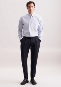 Camicia button-up a scacchi blu chiaro, pantaloni tailored scuri e scarpe stringate nere. La camicia è dotata di colletto e maniche lunghe, con un taglio aderente.