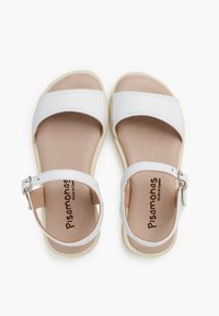 White sandals with a smooth synthetic upper, wide straps, adjustable ankle buckle, and a soft beige insole on a textured rubber sole.