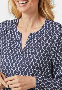 Navybluse mit einem weißen geometrischen Muster, V-Ausschnitt und gerafften Bündchen. Glattes Material mit subtiler Struktur und lässiger Passform.
