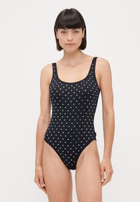 Black one-piece swimsuit featuring a scoop neck and thick straps, covered with white polka dots. Smooth texture and high-cut leg design.
