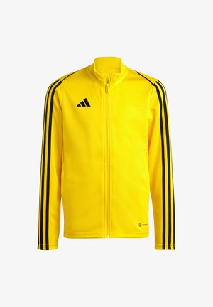Giacca gialla con zip, realizzata in materiale liscio, con strisce nere sulle spalle e sulle maniche, caratterizzata da un logo Adidas sul petto.