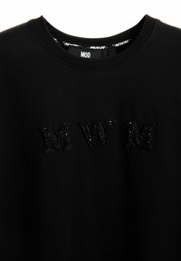 Camiseta de algodón negra con las letras "MWM" en cuentas negras texturizadas, cuello redondo y una etiqueta que dice "MOD" dentro del cuello.