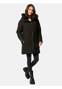 Black padded coat with a hood, featuring a buttoned front, side pockets, and ribbed cuffs. Worn over dark jeans and black ankle boots.