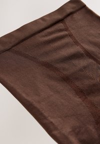 Smeđa rebrasta tkanina s uzorkom teksture u obliku cik-cak uzorka i glatkim dijelovima, preklopljena na neutralnoj pozadini.