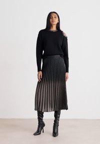 Μαύρο πλεκτό πουλόβερ με λεπτομέρειες στους ώμους, σε συνδυασμό με μαύρη πλισέ φούστα με κλιμακωτή γυαλάδα και ψηλοτάκουνα μποτάκια.