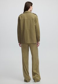 Chaqueta verde oliva y pantalones a juego de tejido suave. La chaqueta presenta un cuello clásico y puños abotonados. Diseño holgado con una textura suave.