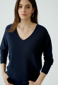 Pull en tricot bleu marine avec un décolleté en V profond, des manches longues et une coupe décontractée. Tissu texturé, design minimal, adapté à un style décontracté.