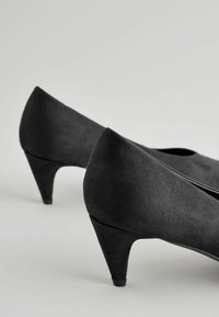 Czarne zamszowe buty na wysokim obcasie o zwężającym się kształcie i teksturowanej powierzchni; mają skromny obcas i elegancką sylwetkę.