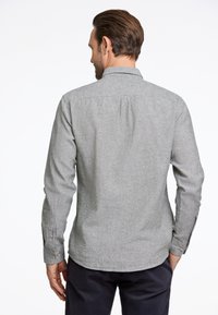 Camicia grigia a maniche lunghe con una trama sottile, colletto classico e polsini abbottonati. La piega posteriore aggiunge una vestibilità rilassata.