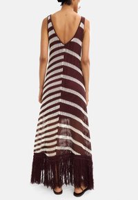 Szydełkowa sukienka maxi w głębokim burgundzie i kremowych paskach, z głębokim dekoltem na plecach, luźnym krojem oraz frędzlami na końcu, które dodają tekstury.