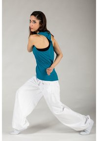 Teal sleeveless top with draped back, paired with loose-fitting white trousers. In-motion pose, with a textured, casual design.