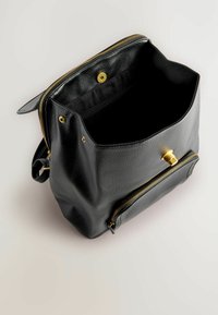 Schwarzer Leder-Rucksack mit offenem Hauptfach, goldenem Reißverschluss und Verschluss, vordere Reißverschlusstasche, vor hellem Hintergrund.