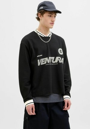 Sweatshirt negru cu mânecă lungă, textură cu nervuri, gât rotund, accente albe și imprimeu grafic cu textul "VENTURA". Asortat cu pantaloni scurți cargo de culoare închisă.