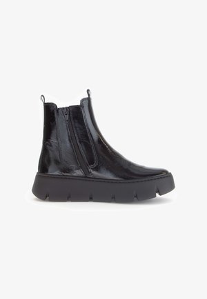 Schwarze, glänzende Knöchelstiefel mit seitlichem Reißverschluss, dicker strukturierter Sohle und Ziehschlaufen auf einem weißen Hintergrund.