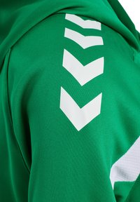 Tissu vert avec trois formes de chevrons blancs angulaires alignés verticalement, et une partie d'une bande texturée blanche sur le côté droit.