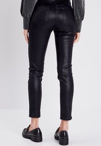 Zwarte, glanzende skinny pants met een gladde textuur, twee achterzakken en een enkel-lange pasvorm, gecombineerd met zwarte, gestructureerde loafers.