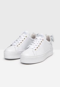 White leather sneakers with a platform sole, featuring gold eyelets, white laces, and a bow accent on the heel, smooth texture.