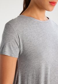 Szary prążkowany t-shirt z krótkimi rękawami, okrągłym dekoltem i rozcięciami po bokach. Miękka tekstura i luźny krój, odpowiedni do codziennego noszenia.