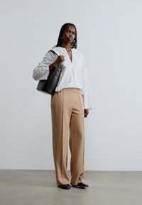 Λευκό, πουκάμισο με γιακά και μακριά μανίκια, με v-λαιμόκοψη· μπεζ, καλοραμμένο παντελόνι· μαύρη τσάντα χειρός· σκούρα παπούτσια· μινιμαλιστικός σχεδιασμός, απαλή υφή.