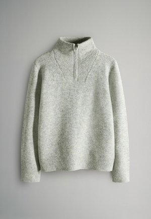 Ljust grått stickat pullover med hög krage och halvdragkedja. Har ribbad textur på kragen och ärmarna, med en något lös passform.