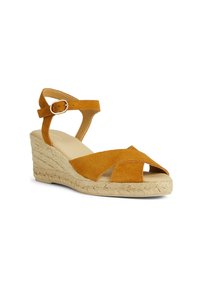 Infradito in suede con zeppa color giallo senape, design incrociato nella parte anteriore, cinturino alla caviglia regolabile e tacco in corda intrecciata.