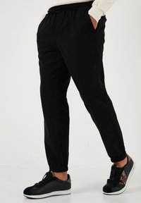 Schwarze Jogginghosen mit elastischem Bund, seitlichen Taschen und schmal zulaufenden Bündchen. Getragen mit schwarzen Turnschuhen, die ein strukturiertes Design und Akzente aufweisen.