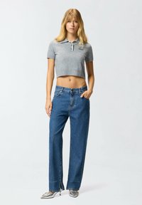 Siva skraćena polo majica s kratkim rukavima, uparena s visokim strukom, širokim plavim trapericama i metalik šiljastim potpeticama.