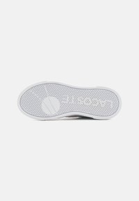 Valge kummist kinga tald kuue nurga mustriga, millel on embosseeritud sõna "Lacoste". Kujundus on ühtlane ja ümarate varvastega.