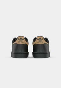 Black leather sneakers with tan accents, featuring a rounded toe, flat black rubber sole, and embossed brand logo on the back.