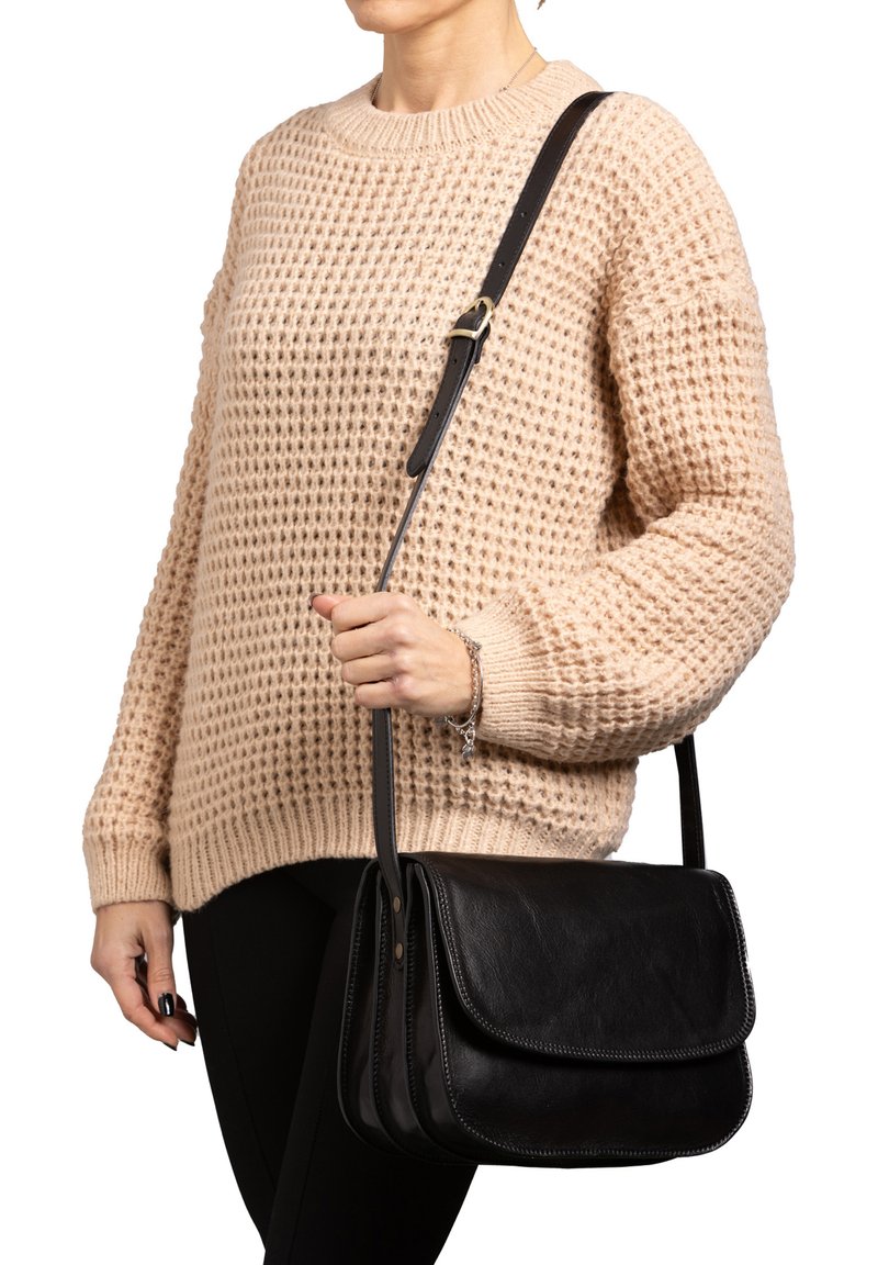 Borsa a spalla in pelle nera con due alette, dettagli cuciti e tracolla regolabile, tenuta contro un maglione a maglia testurizzata.