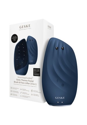 Brosse faciale sonique en bleu foncé, avec un design texturé, deux boutons et une forme élégante, emballée dans une boîte blanche avec des détails de marque.
