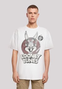Bílý bavlněný tričko s velkým grafickým motivem Bugse Bunnyho s sluchátky a textem "LOONEY TUNES" pod ním, krátké rukávy a uvolněný střih.