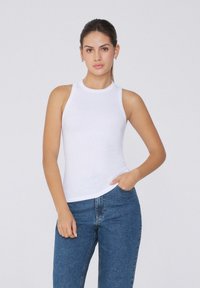 Canotta bianca a costine con scollo alto, forma aderente e senza motivi visibili, abbinata a jeans in denim blu.