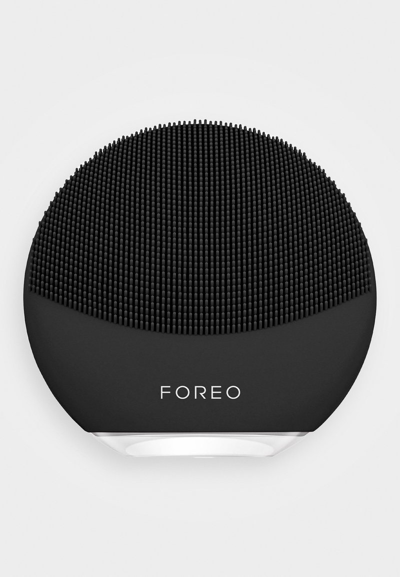 Svart silikon ansiktsrensingsenhet med en teksturert overflate av små, runde nupper og et sirkulært design, med en hvit bunn.