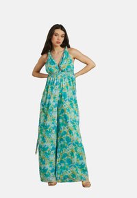 Robe longue sans manches avec un motif abstrait bleu et vert, dotée d'un décolleté en V et d'une taille froncée. Présente une silhouette fluide et des fentes sur les côtés.