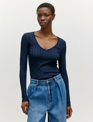 Marineblauw langermanige top met V-hals en verticale ribbeltextuur, gecombineerd met lichtblauwe denimbroek met hoge taille en een oversized pasvorm.