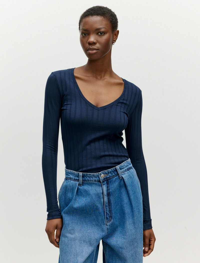 Marineblaues Langarmoberteil mit V-Ausschnitt und vertikal gerippter Textur, kombiniert mit hochgeschnittenen, hellblauen Jeanshosen im Oversized-Stil.