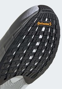 Suela de zapato negra texturizada con un patrón de espiga. Presenta un logo de Continental en naranja cerca del talón. Parte superior en gris.